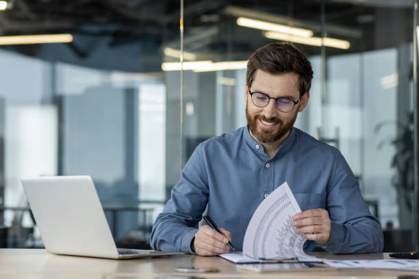 istock Smiling businessman working on documents and laptop in modern office 2167850210