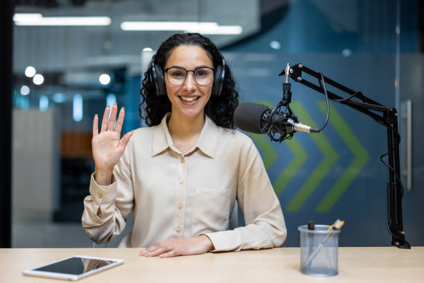 istock Friendly podcast host in studio waving to camera, inviting audience to a live session 2167850851