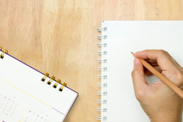hand writing in a notebook with pencil on wood table.