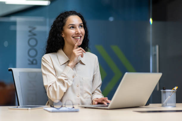 istock Businesswoman thinking and smiling while working on laptop in modern office 2167851866