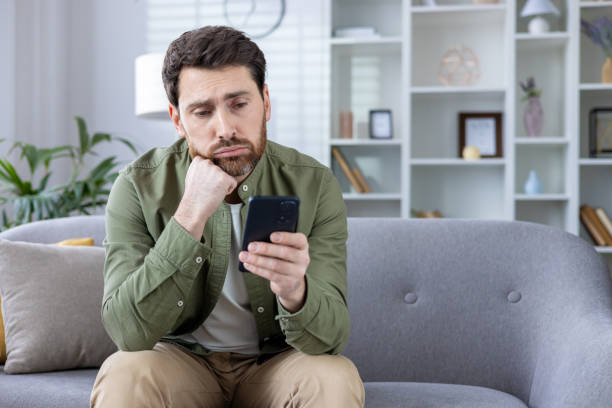 istock Thoughtful man sitting on sofa looking at smartphone at home 2167852468