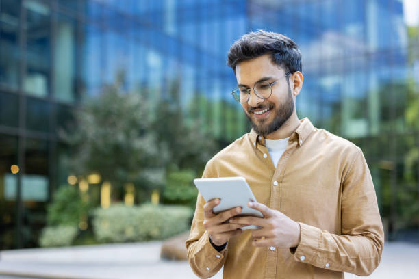 istock Young man using tablet outside modern office building, smiling and reading 2167853210
