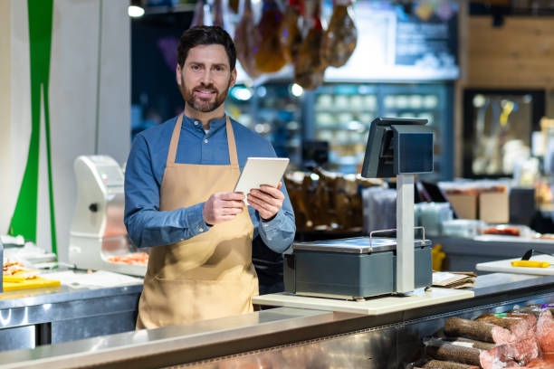 istock Smiling shopkeeper using digital tablet at delicatessen counter in modern grocery store with pleasing ambiance 2167856632