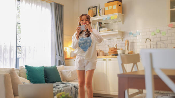 Asian freshness young woman with casual feeling excited while listening and dancing to energetic music with headphones at home. Cheerful female having fun while moving and grooving to her favourite songs she singing from lylic in smartphone asian freshness young woman with casual feeling excited while listening and dancing to energetic music with headphones at home. cheerful female having fun while moving and grooving to her favourite songs she singing from lylic in smartphone