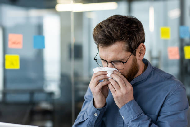 Man sneezing in office using tissue due to cold or allergies