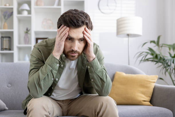 istock Stressed man sitting on a sofa holding his head, feeling overwhelmed and anxious 2167858185