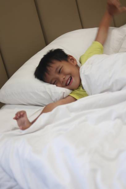 istock Cheerful asian boy stretching after waking up. white blanket. copy space. 2167859215