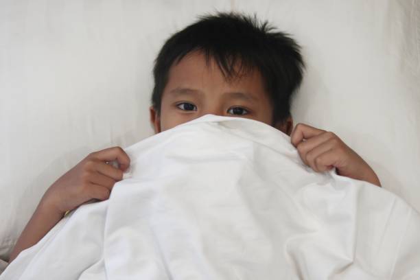 Young Asian Boy Peeking from the white blanket on the bed