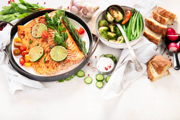 istock Grilled salmon and vegetables on wooden light background. Dinner table with cooked fish, tomatoes, asparagus 2167859447