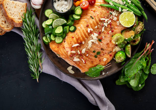istock Cooked salmon with fresh vegetables, lime and souce. Baked fish on dark background 2167859683