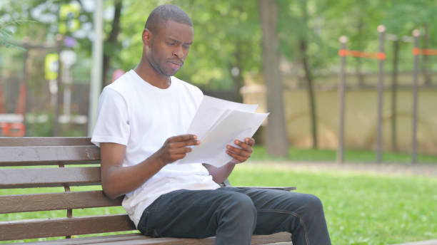 istock Outdoor Sitting Young African Man Reading Documents 2167860069