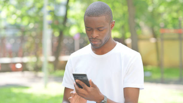 istock African Man Text Messaging on Phone Outdoor in Park 2167860084