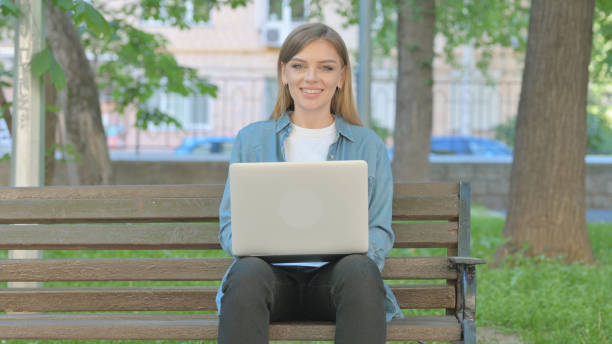 istock Woman with Laptop Smiling at Camera while Sitting on Bench in Park 2167861268