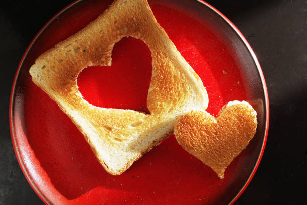 Slice of breads with jam in shape of heart, and raspberries over brown wooden table. Love concept with copy space.