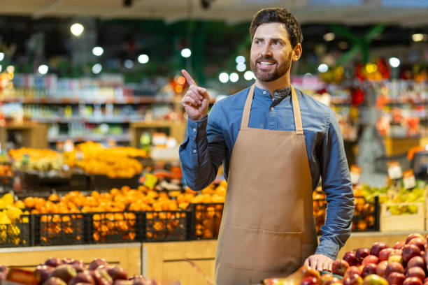 Smiling grocery store worker pointing while standing in produce section