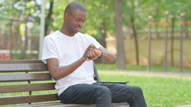 istock Young African Man Using Smartwatch while Sitting Outdoor on Bench 2167862941