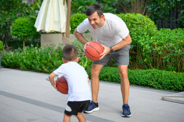istock Father coaches his young son on basketball technique amidst lush greenery. 2167863247