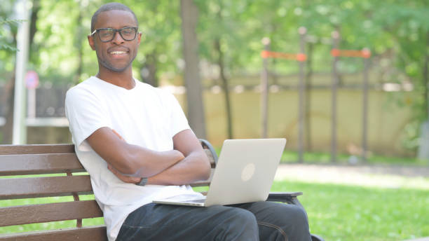 istock Young African Man Smiling at Camera while Using Laptop Outdoor 2167864845