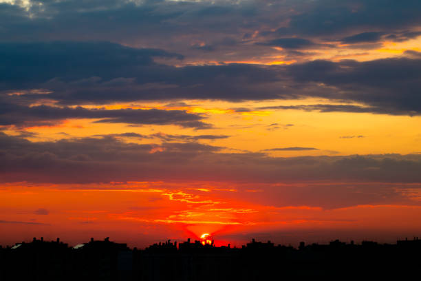 Cloudy sky above silhouettes of buildings. Sunset sun in clouds above city rooftops