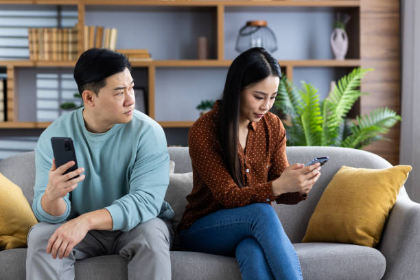 Asian couple on a couch both using smartphones, showing technology and relationship dynamics