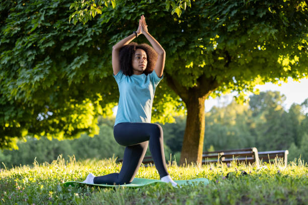 African American woman practicing yoga outdoors in nature under a tree