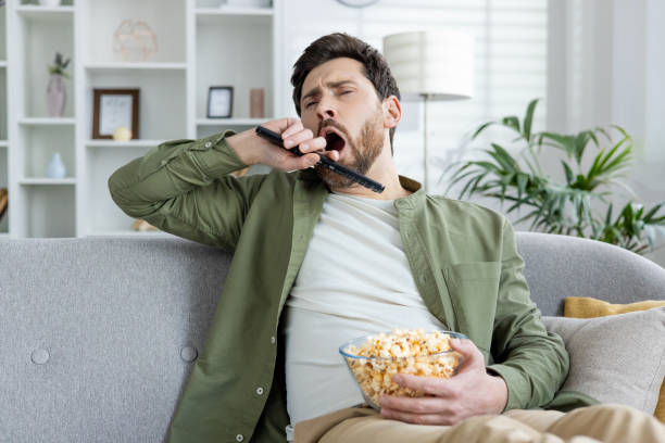 istock Bored man yawning with a remote and popcorn on sofa 2167878717