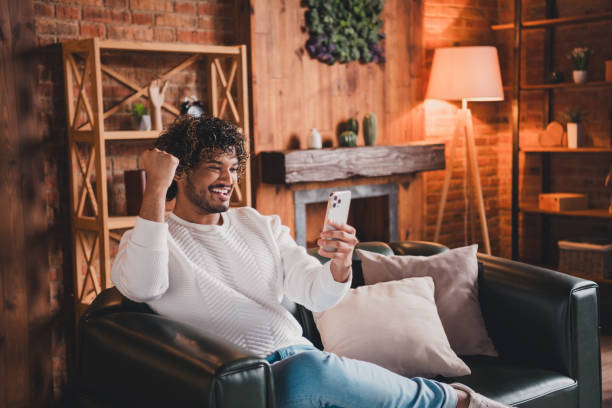 istock Photo of cheerful lucky guy dressed white pullover winning game modern gadget indoors house apartment room 2167883400