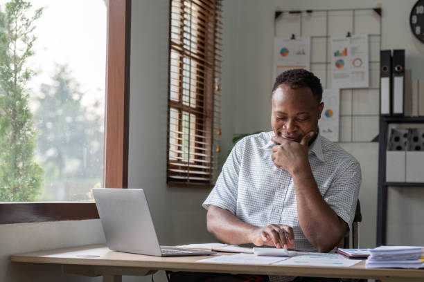 istock American Businessman Analyzing Financial Graph Documents at Home Office Desk with Laptop and Natural Light 2167885851