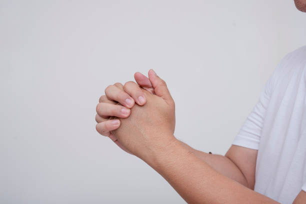 Close-up view of an anonymous man's clasped hands in prayer against a plain white background, depicting faith and spirituality.
