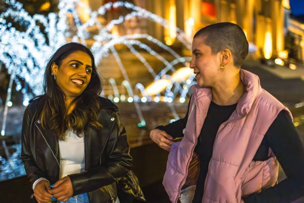 Two friends share a moment of laughter and conversation in front of a beautifully illuminated fountain at night. Upper West side, Manhattan. NYC