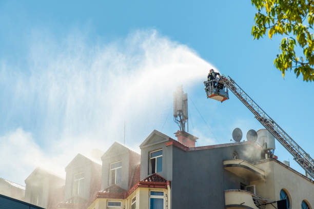 istock Firefighters extinguish burning house using extended ladder equipped with water hose to spray water onto the building roof with smoke. Fireman extinguishing fire in the city 2167890957