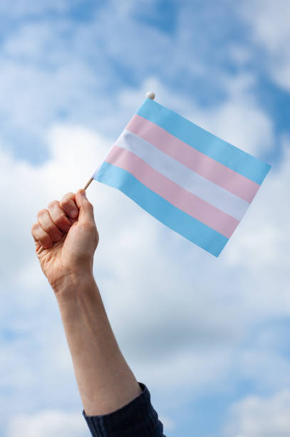 istock Hand holds up transgender pride flag against sky 2167891278