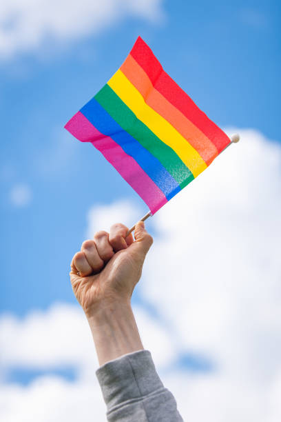 istock Hand holds up rainbow pride flag against sky 2167891279