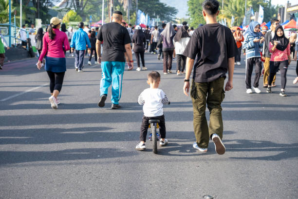 padang,indonesia-21 july 2024:A young boy rides a bicycle on a city street while adults walk in the background.