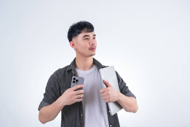 istock Handsome Asian man holding smartphone and laptop computer on white background. Concept for advertising, finance business, communication, technology advancement and online shopping. 2167896640