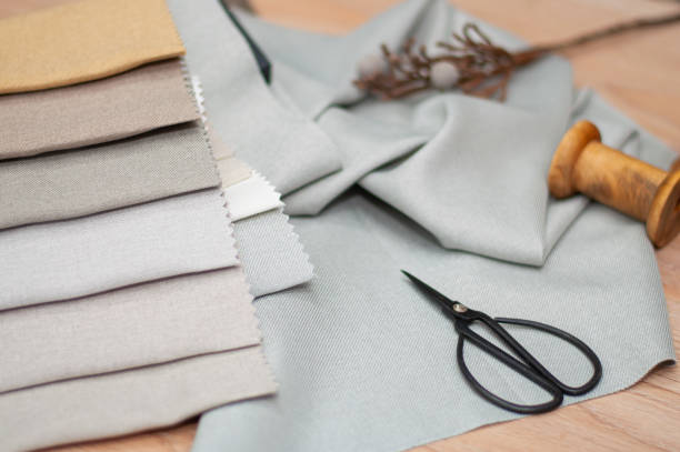 istock Light gray and beige fabric samples, black scissors, wooden thread reel on a brown background. 2167899053