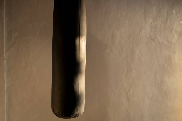 A close-up image of a hanging leather boxing bag against a textured wall in a room.