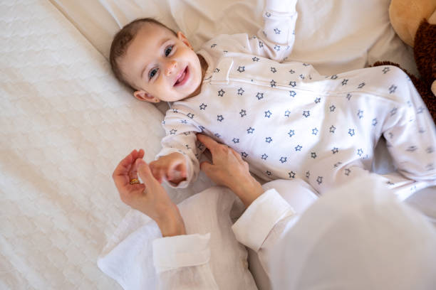 istock Smiling baby in star patterned pajamas lying on a white bed with a teddy bear, being lovingly attended by a parent. Ideal for stock photos on parenting and joy 2167903797