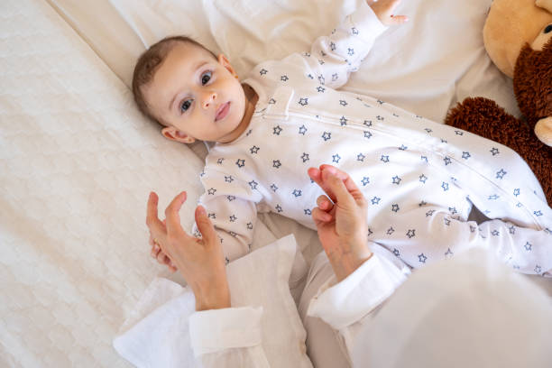 istock Smiling baby in star patterned pajamas lying on a white bed with a teddy bear, being lovingly attended by a parent. Ideal for stock photos on parenting and joy 2167903888