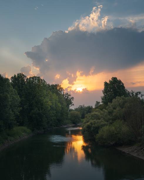 istock Serene river landscape at sunset with a dramatic sky and lush green trees reflecting in the water 2167918283