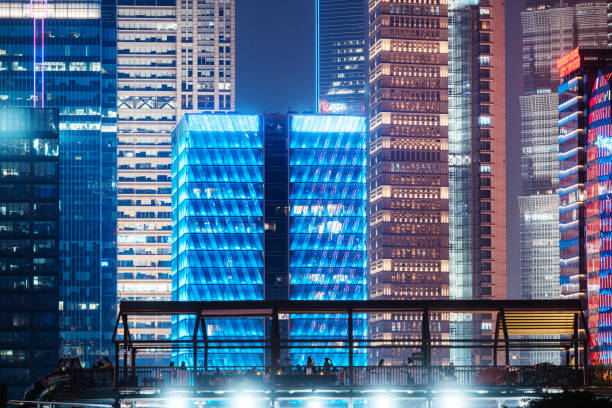 A nighttime view of modern skyscrapers in Shanghai, China, beautifully illuminated with vibrant blue and yellow lights, capturing the essence of urban life and architectural innovation.