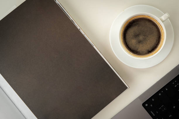 A Stack of Magazines, a Cup of Coffee, and a Laptop on a White Table close up