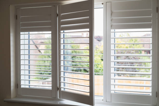 istock Three frames of  white modern wooden shutters across a window. One section is open. The shutter slats are swivelled in different positions. 2167940591