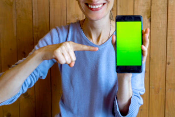 Smiling thin woman shows chromakey on smartphone screen. unrecognizable persona. Close-up. Soft focus, blurred.