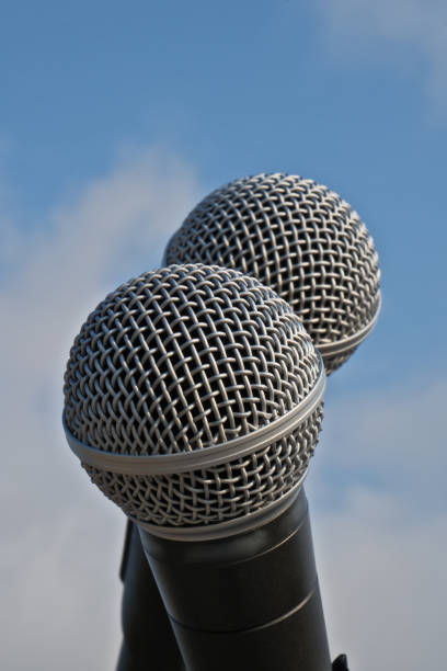 Close up of microphones against a blue sky with white clouds.