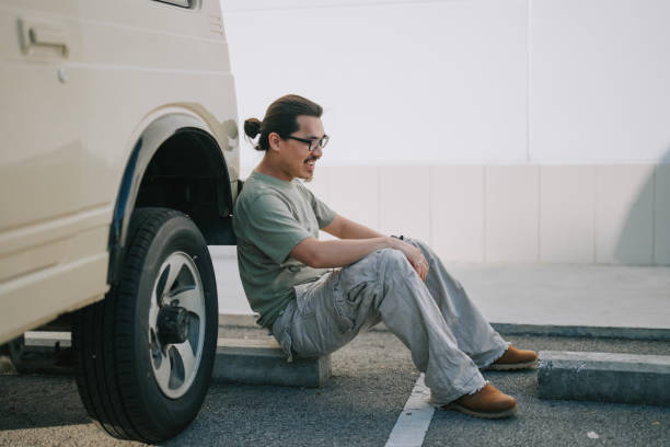 istock Asian Chinese man sitting on ground leaning on SUV laughing 2167950671