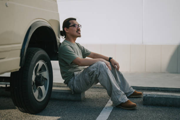 istock Asian Chinese man sitting on ground leaning on SUV laughing 2167950672