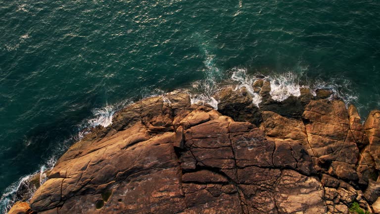 Aerial View of the Turquoise Ocean Waves Crash Against Rocky Coastline, moody sea weaving around boulder-strewn coastlines