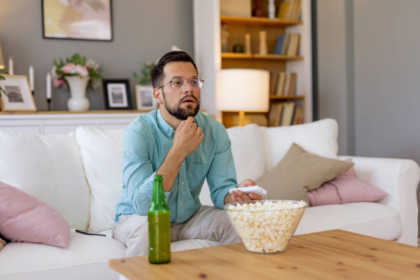 istock Man with remote and popcorn sitting on white couch 2167955453