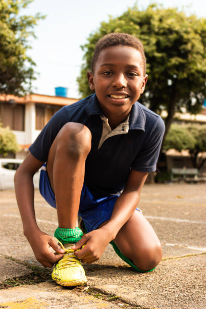 Black Latino boy smiling and looking at the camera while tying his sports shoes on a court in Neiva - Huila - Colombia